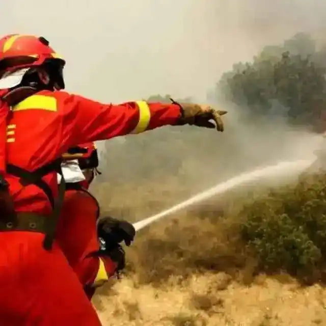 Bombero con traje rojo y casco, manejando manguera contra el fuego