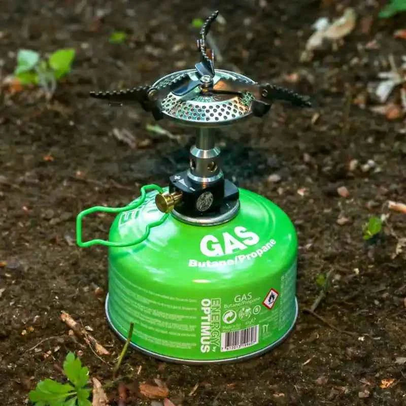 Cartucho de gas Optimus de Mil-Tec de 100g con hornillo portátil acoplado en uso exterior.